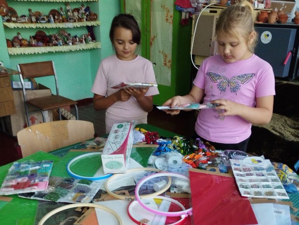 Two girls are sitting at a table with craft supplies.