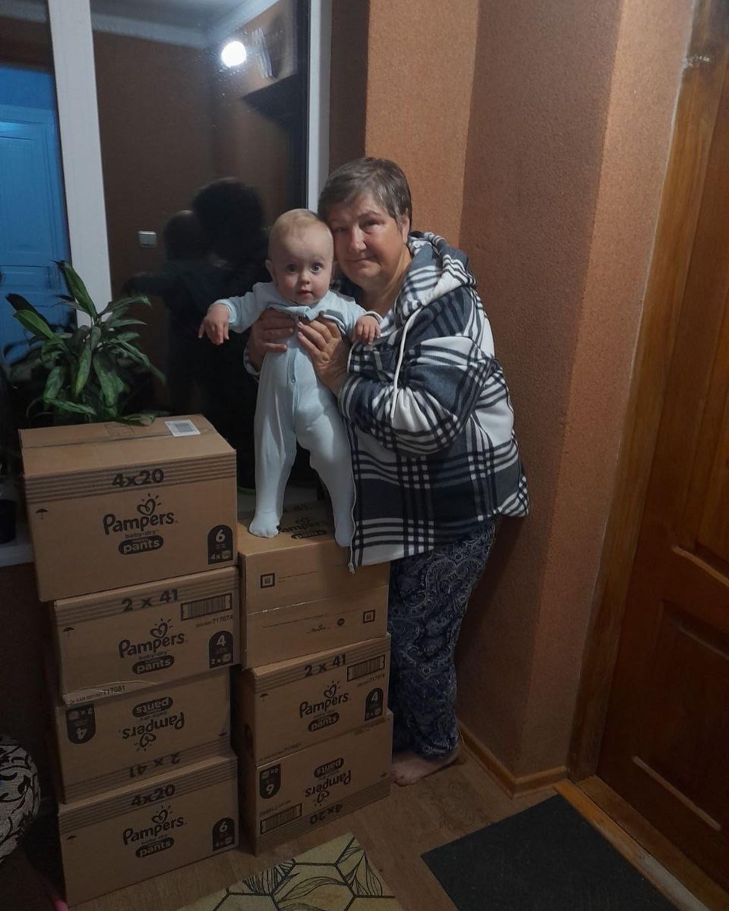 A woman holding a baby in front of a stack of boxes.