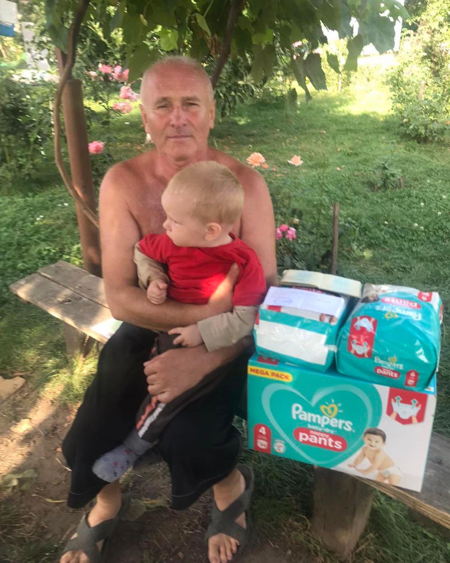 A man sits on a bench with a baby and boxes of diapers.