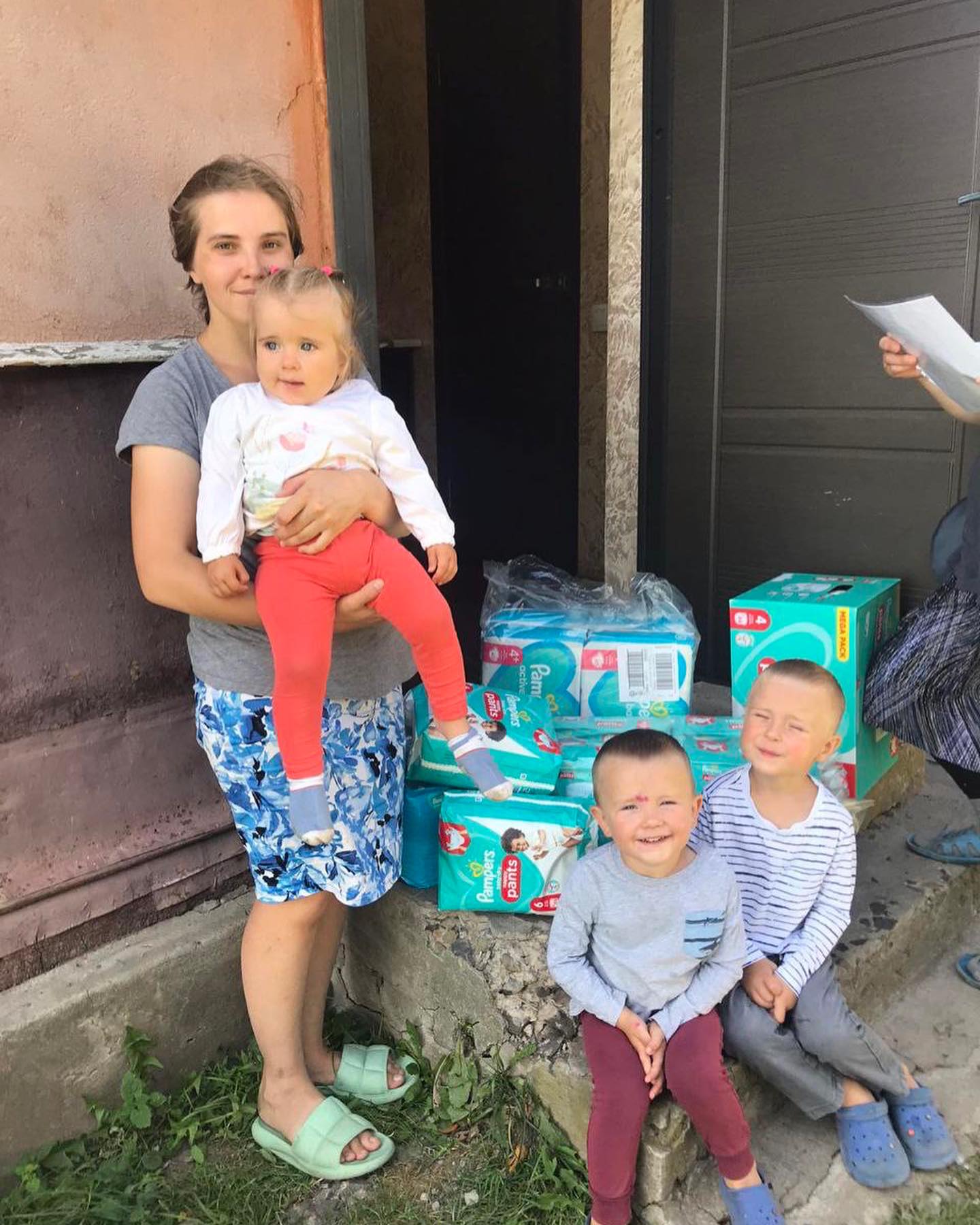 A group of women and children standing in front of a house with boxes of diapers.