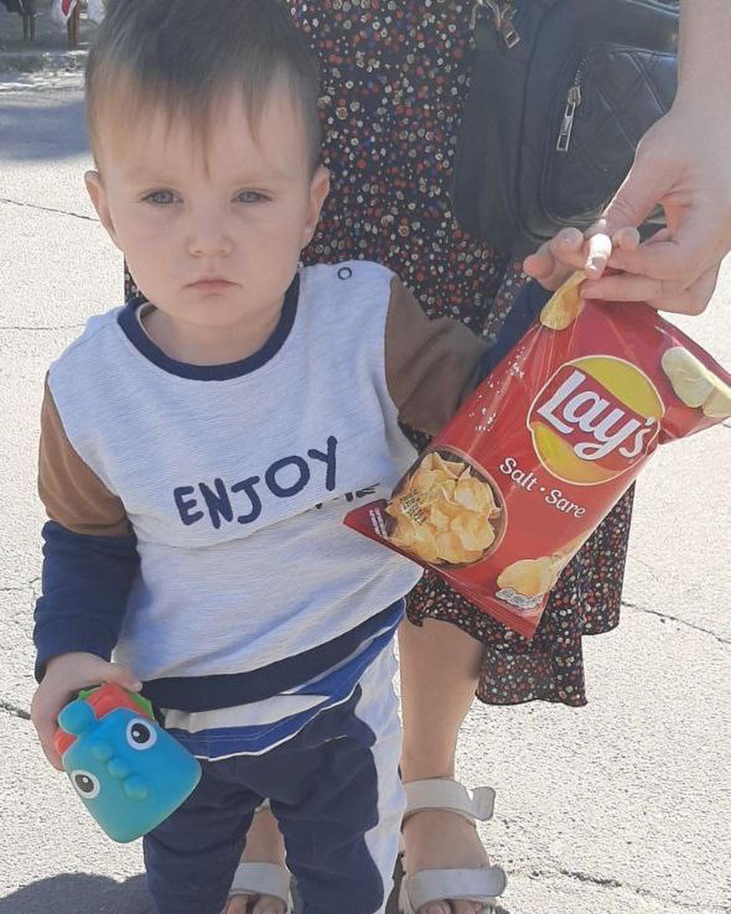 A woman holding a baby holding a bag of chips.