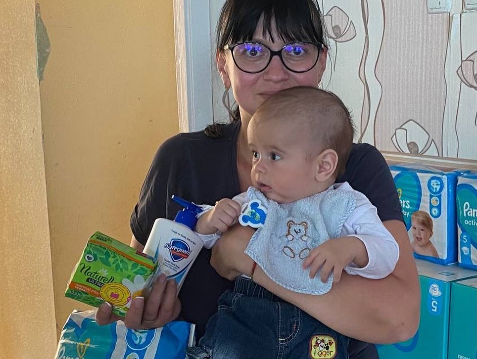 A woman holding a baby in front of boxes of diapers.