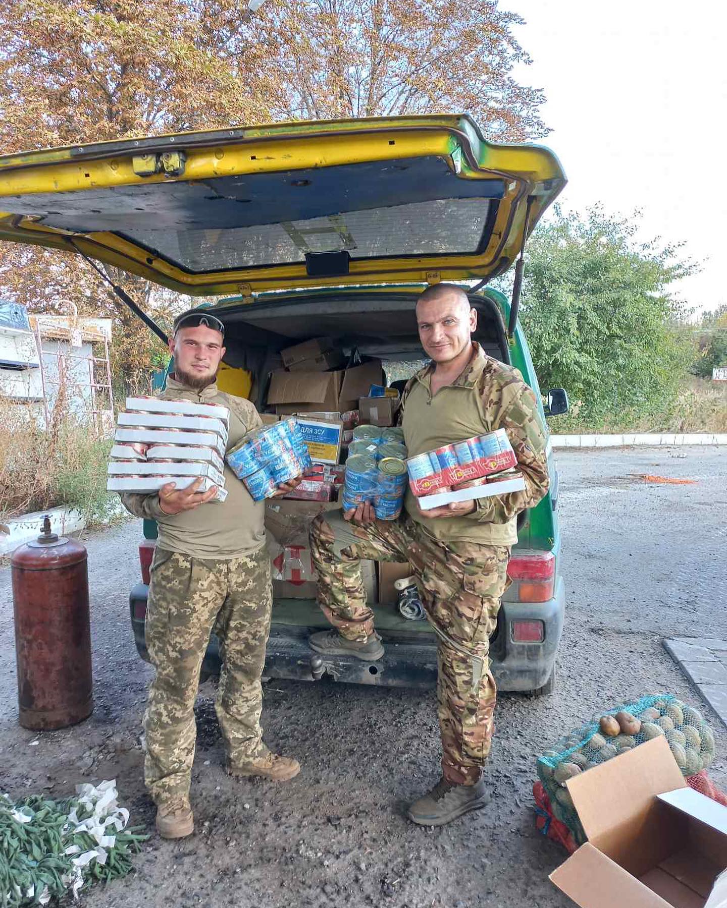 Two men standing next to a van with boxes of food.