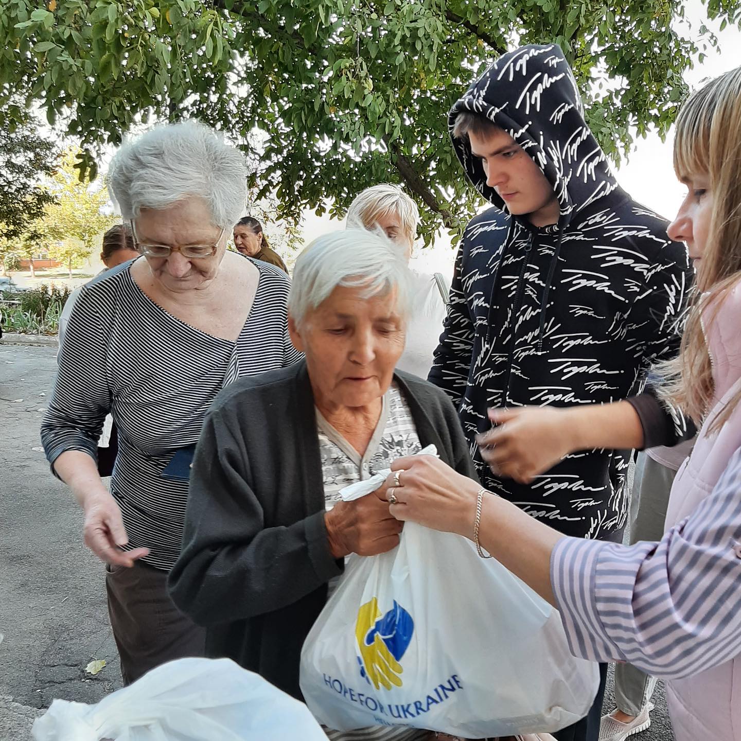 A group of people standing around an older woman with bags.