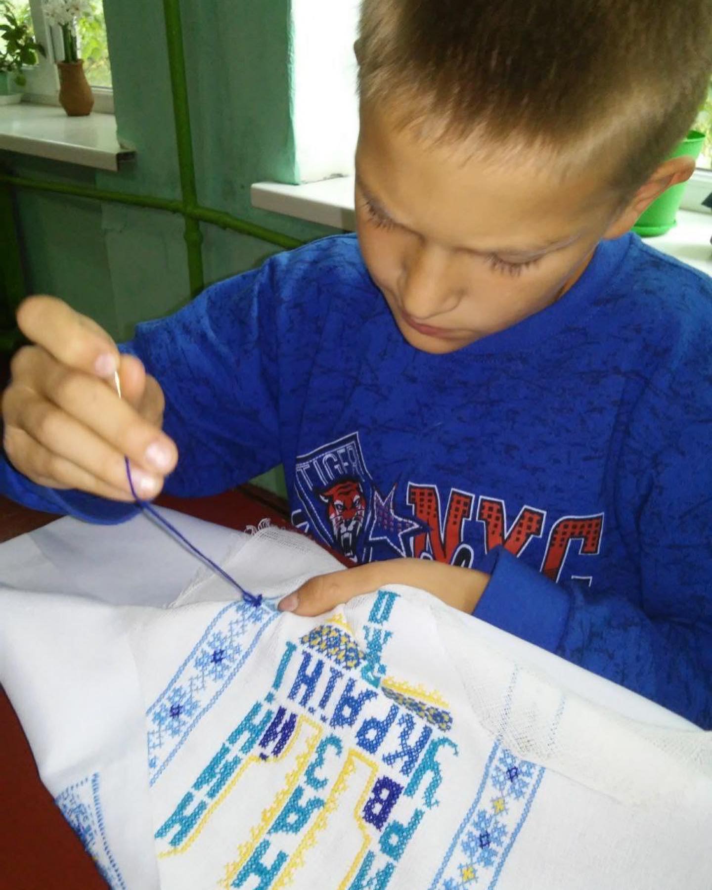 A boy is making a cross stitch on a piece of paper.