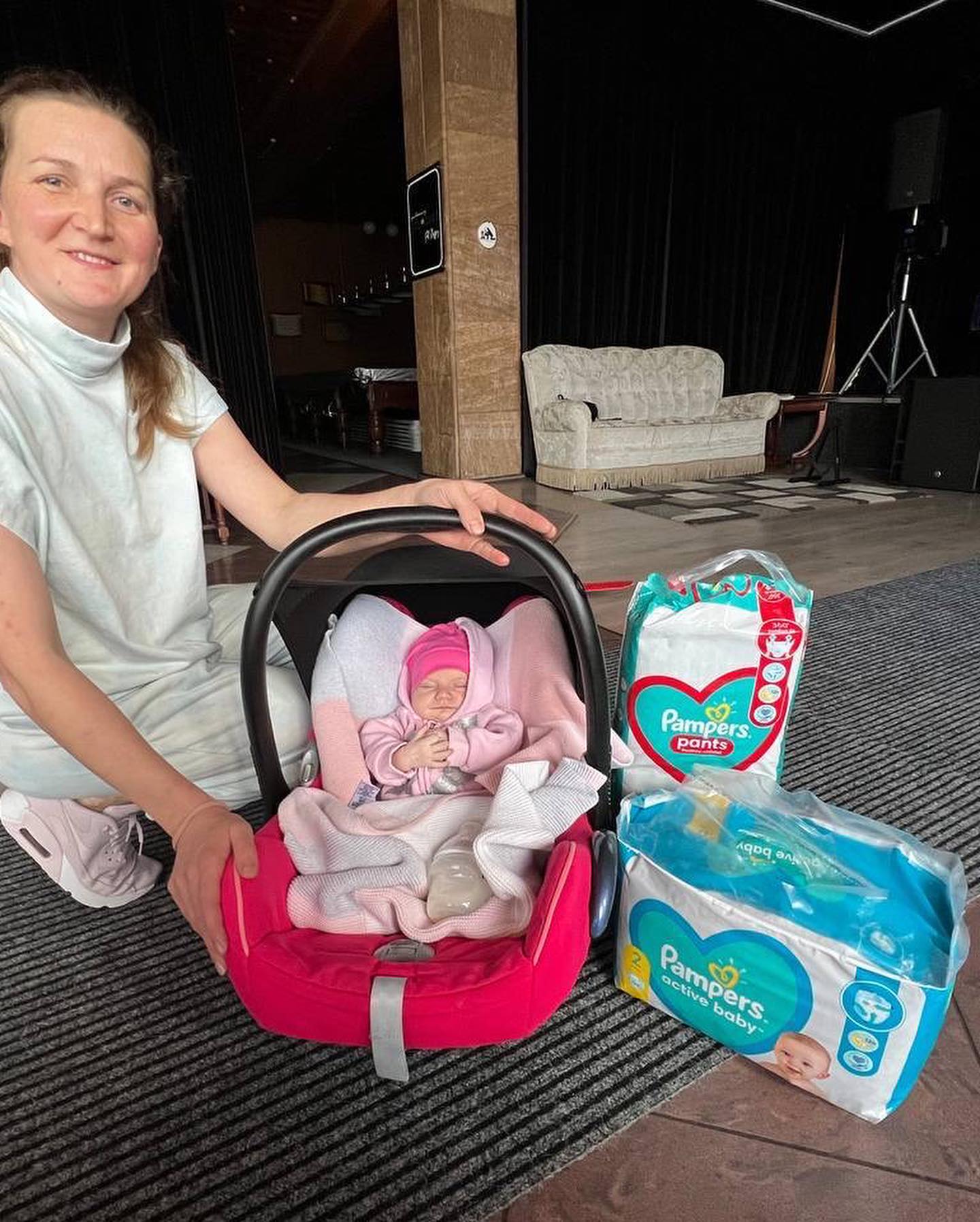 A woman is posing next to a baby car seat and diapers.