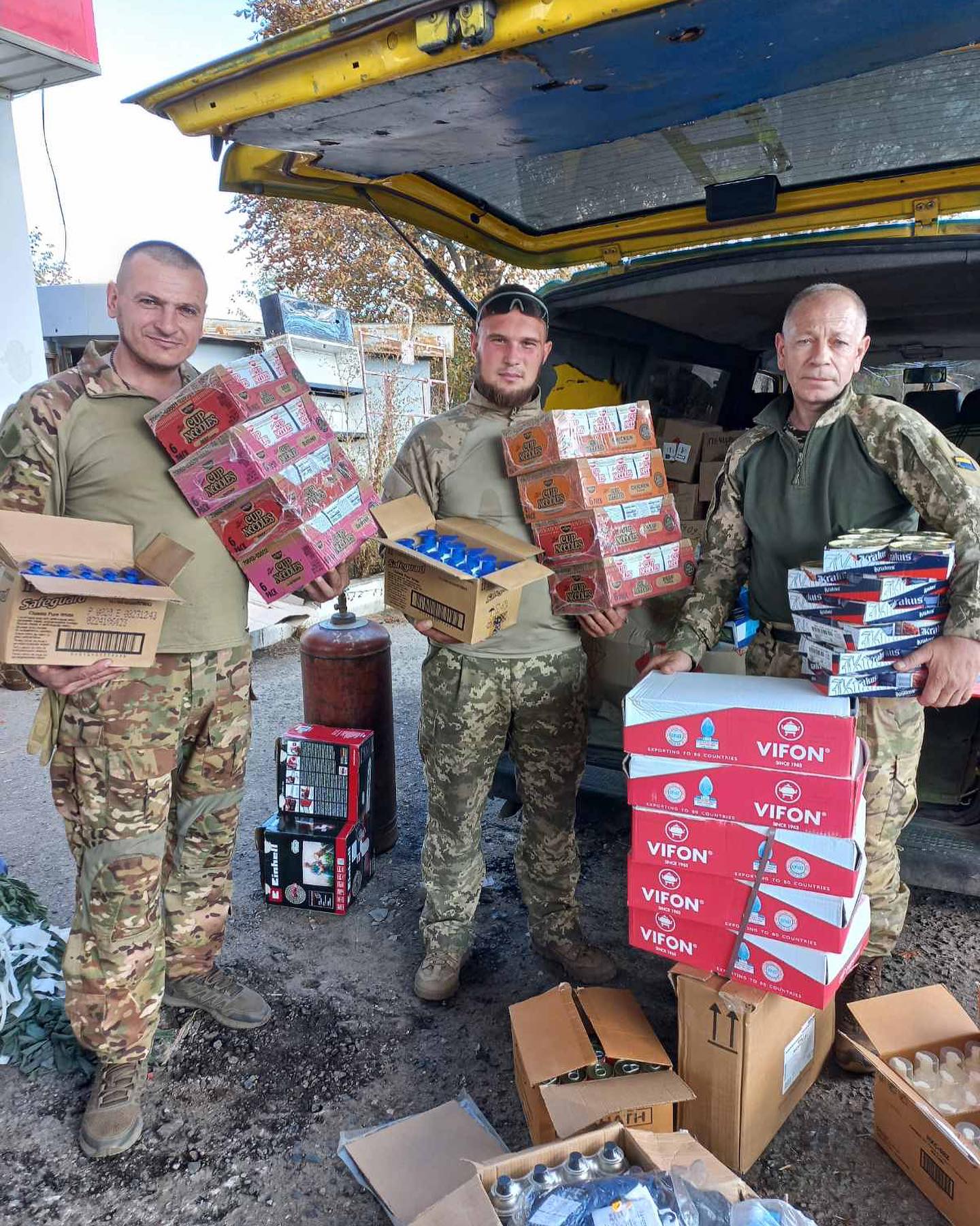 Three men in military uniforms standing next to boxes of food.