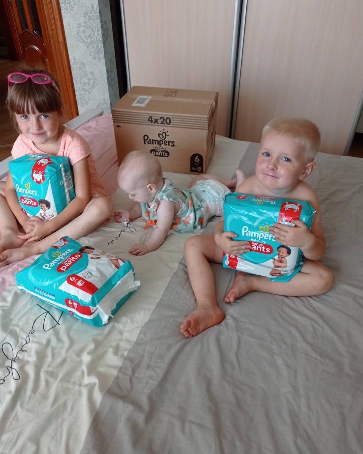 Three small children sitting on a bed with diapers.