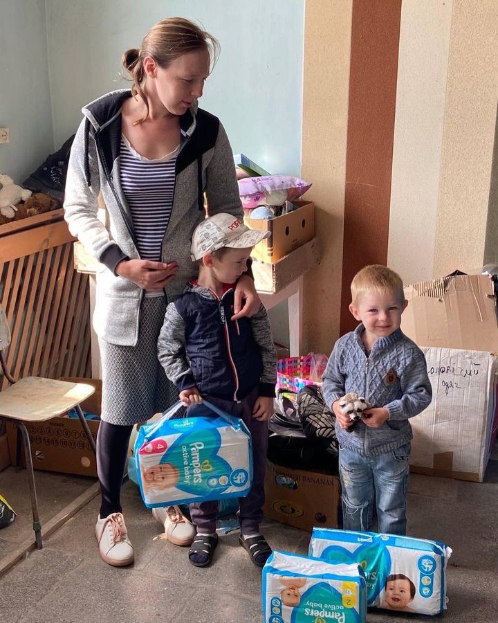 A woman and two children standing next to boxes of diapers.