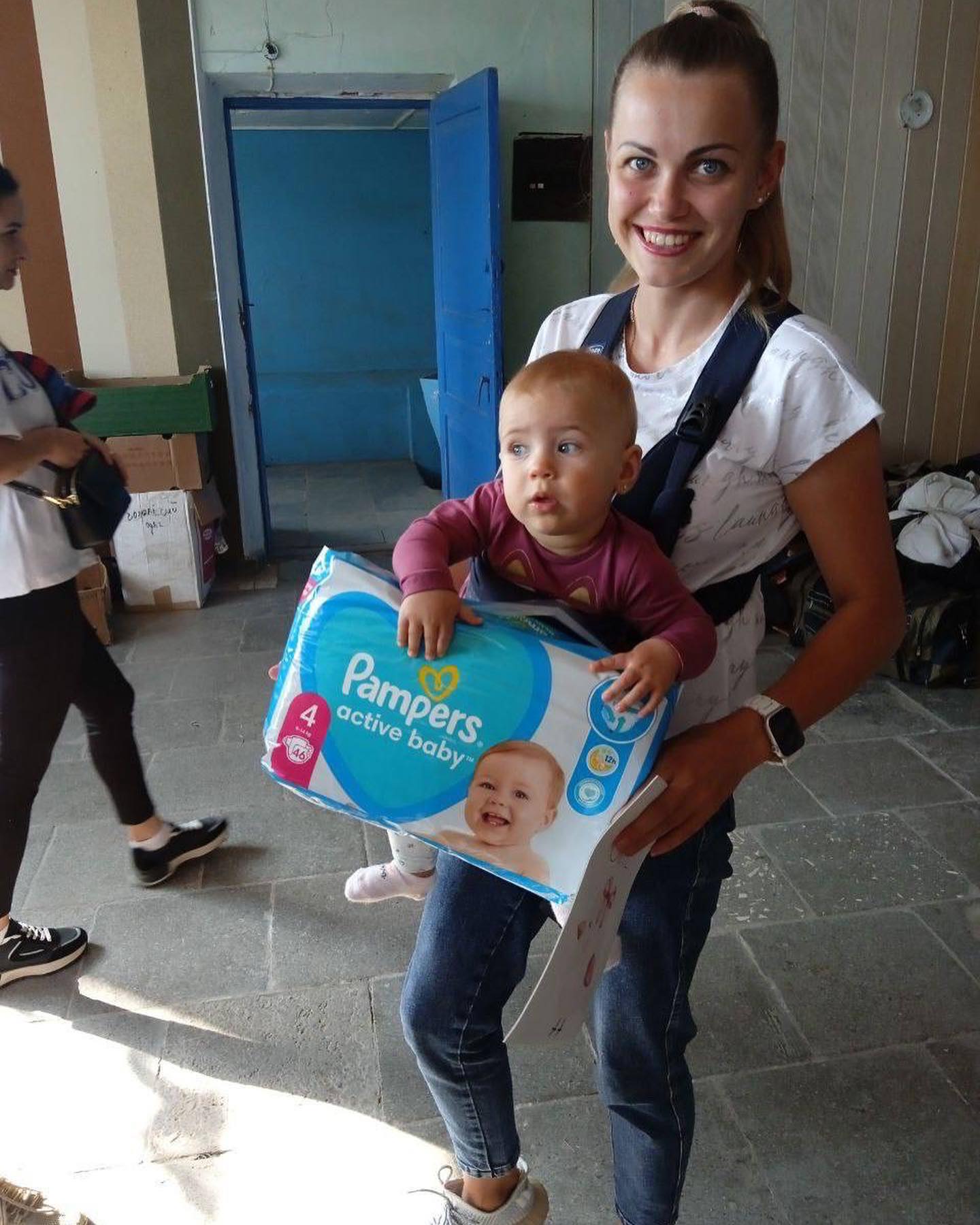 A woman carrying a baby in a diaper box.