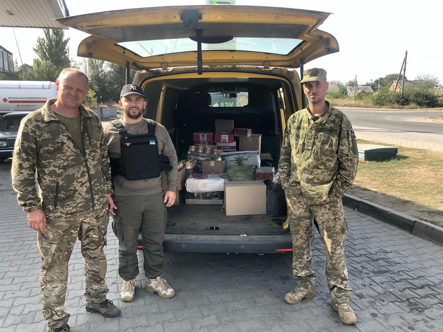Three men in camouflage standing next to a van.