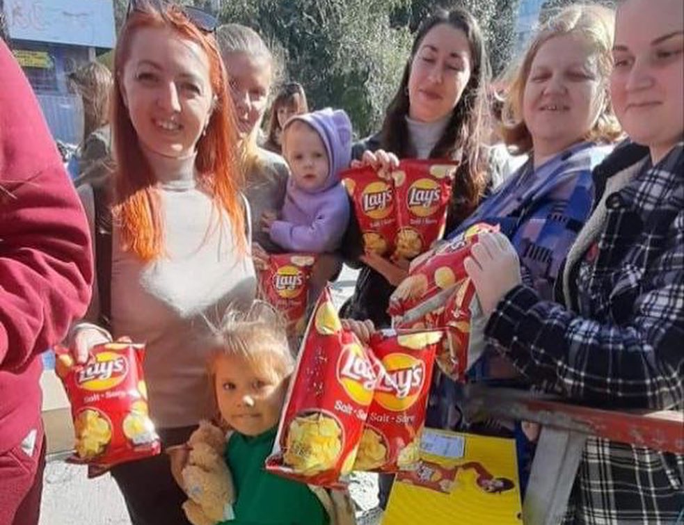 A group of people holding bags of chips and a baby.