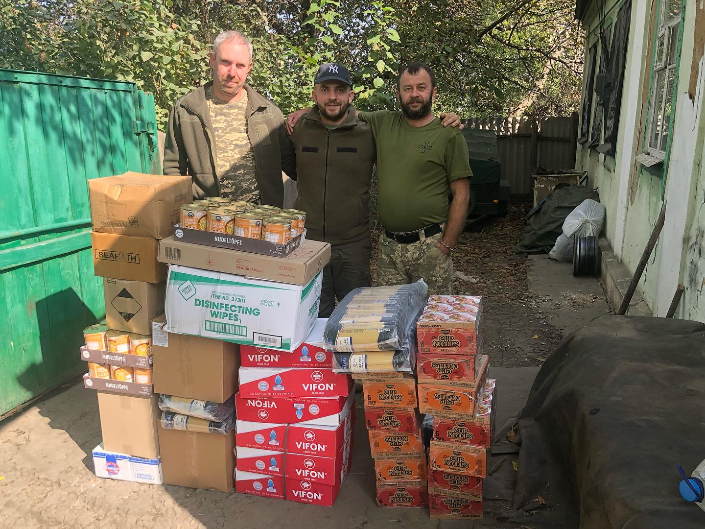 Three men standing next to boxes of food.