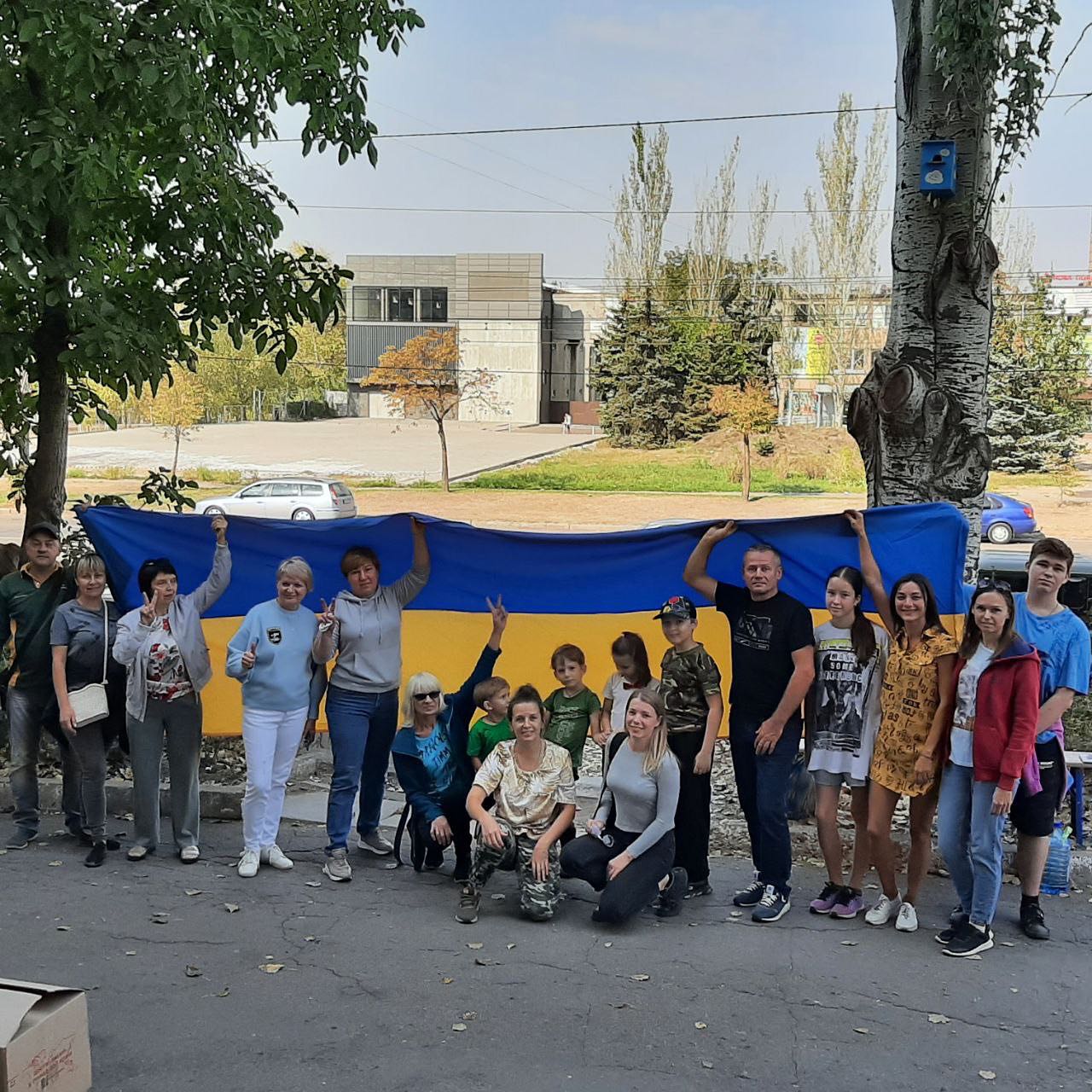 A group of people posing in front of a large ukrainian flag.