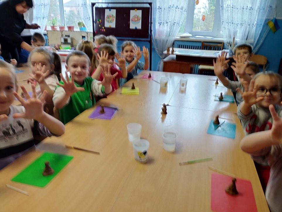 A group of children at a table with their hands up.