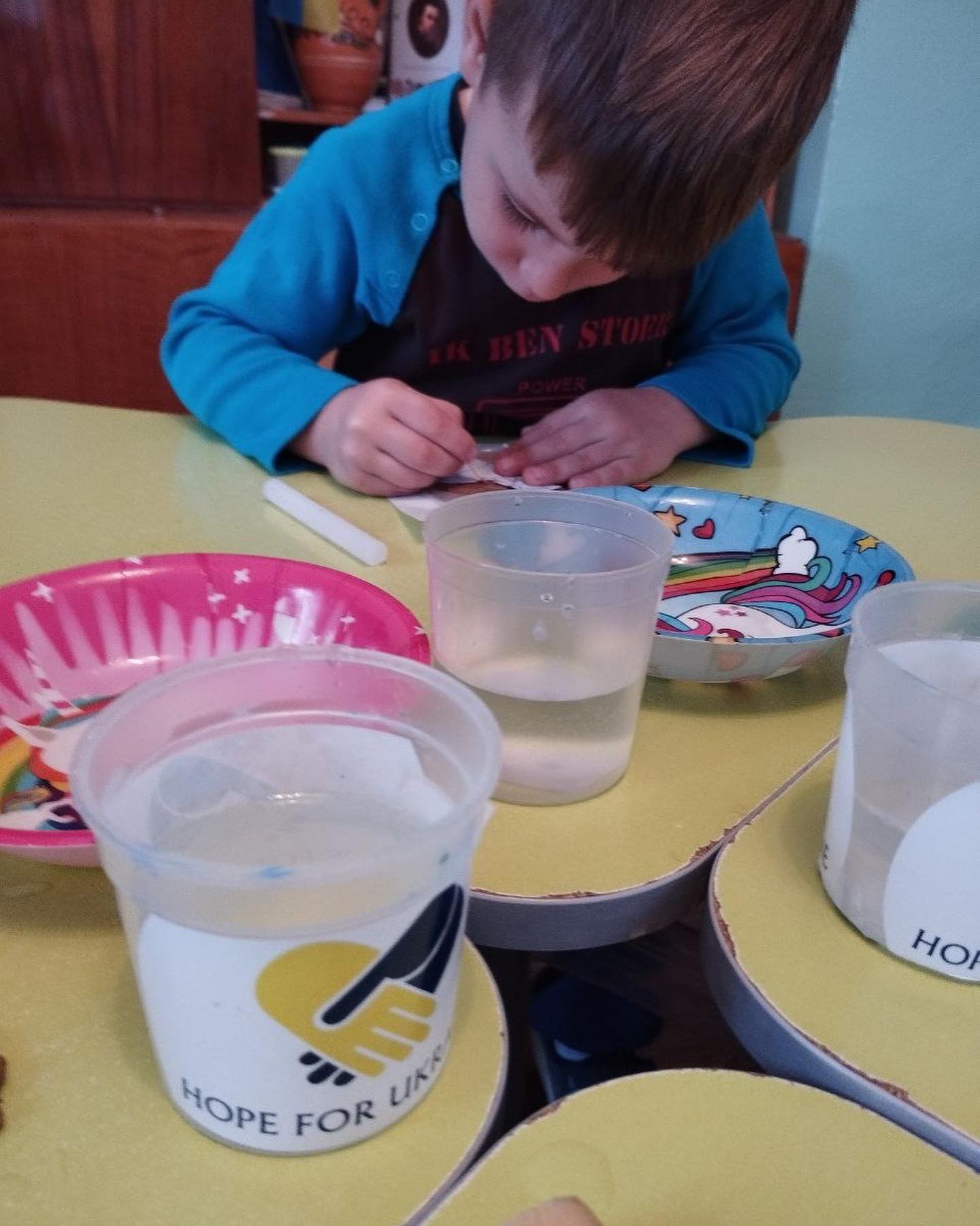 A boy is sitting at a table with cups of water.