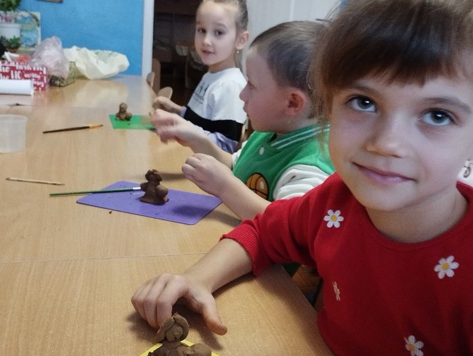 A group of children are sitting at a table making clay figurines.