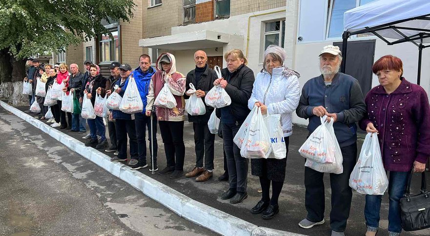 A group of people standing in line with bags of food.