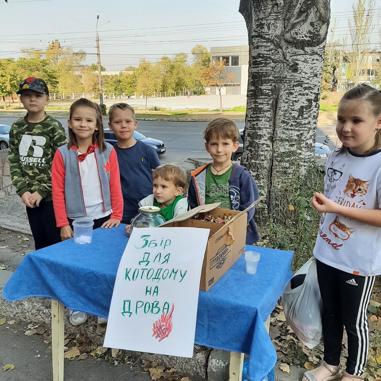 A group of children standing in front of a table with a sign.
