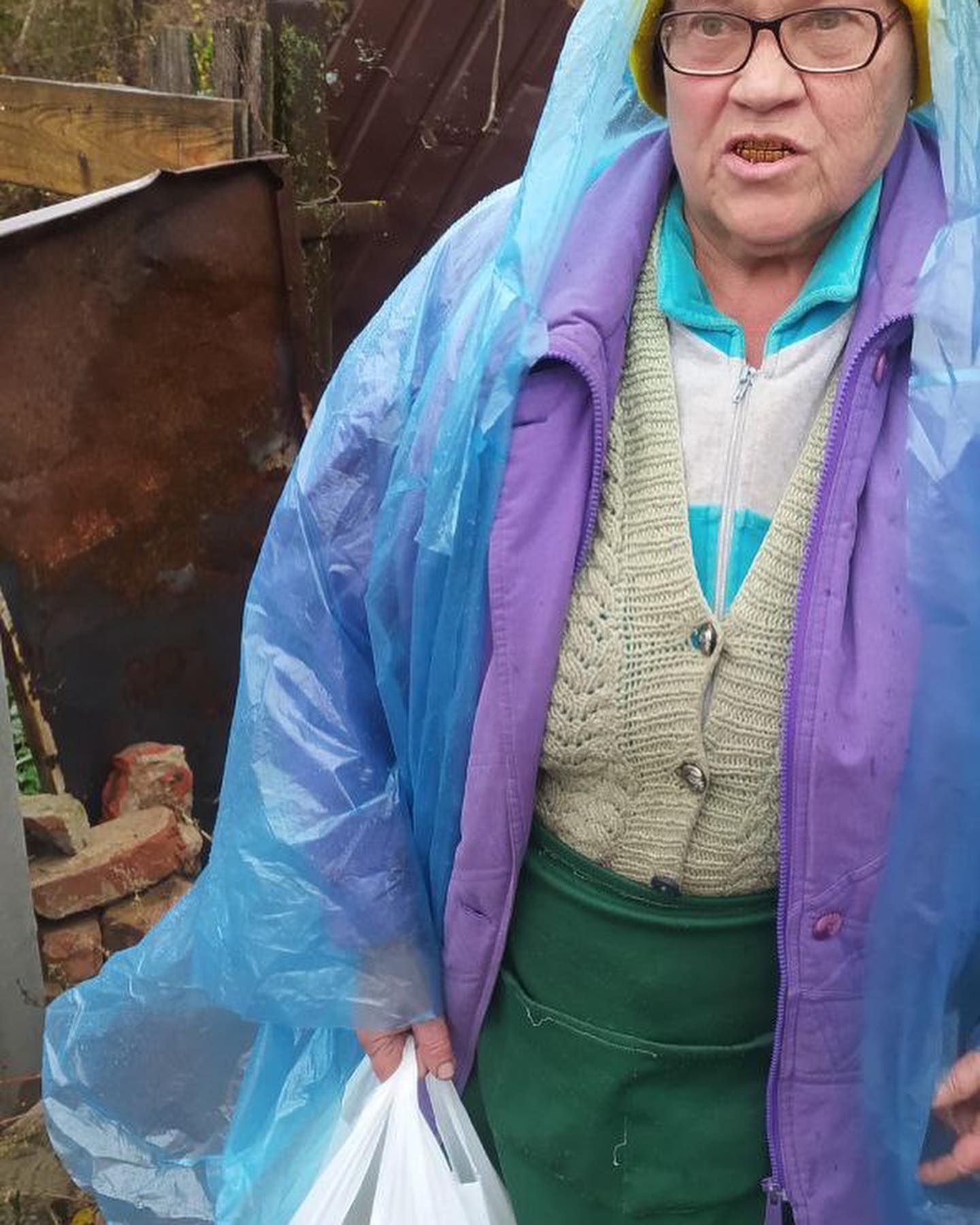 A woman in a blue raincoat standing in a yard.
