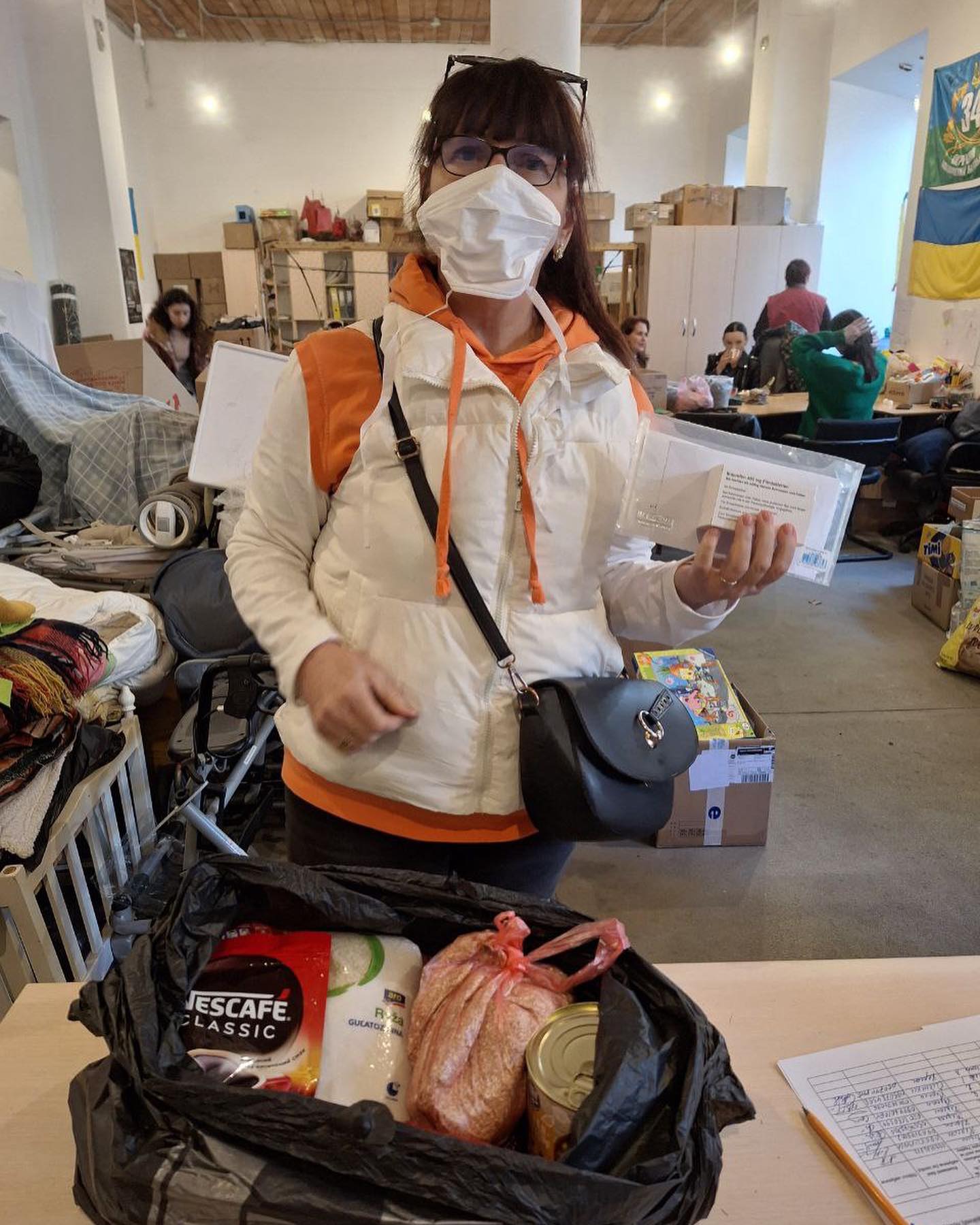 A woman in a mask stands next to a bag of food.