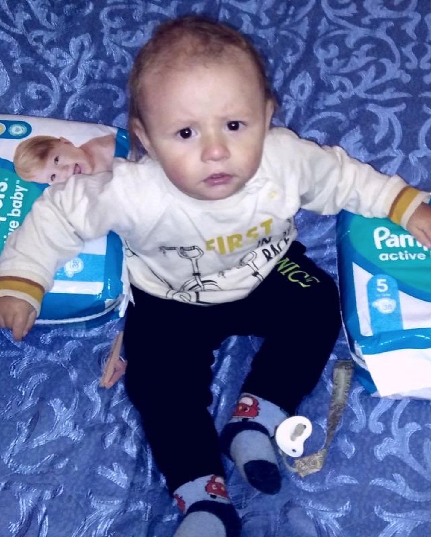 A baby sitting on a bed with a pack of diapers.
