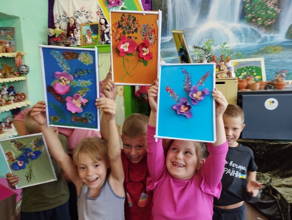 A group of children are holding up pictures of flowers.