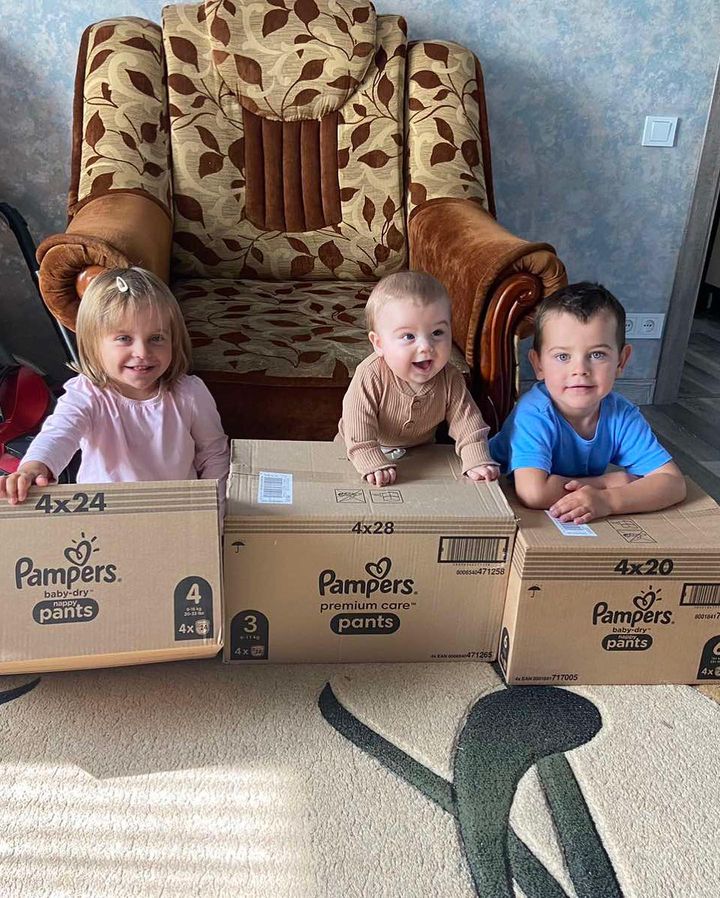 Three children sitting on a couch with boxes in front of them.