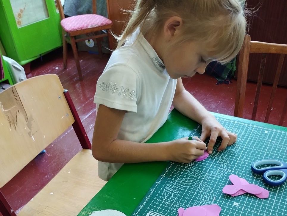 A little girl is cutting paper with scissors at a table.
