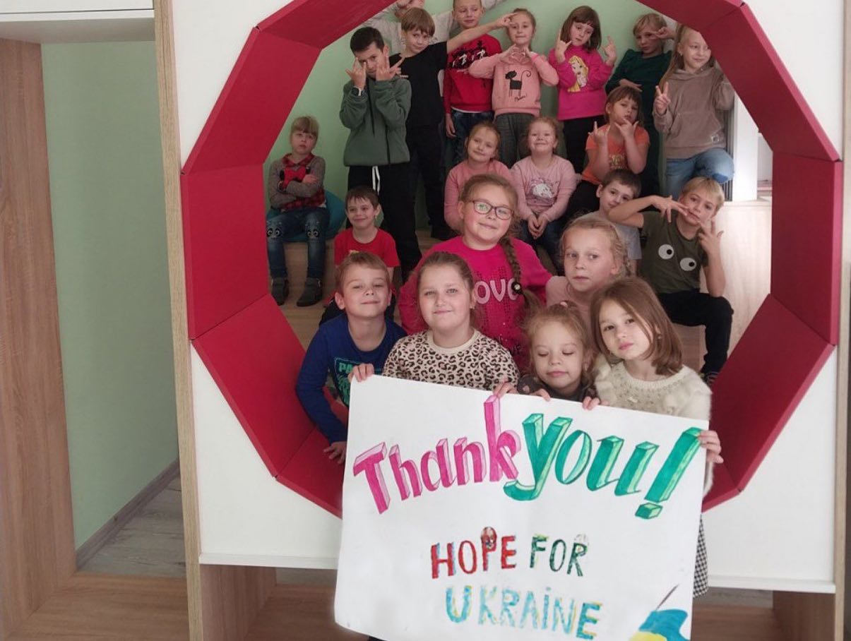 A group of children holding a sign that says thank you home for ukraine.