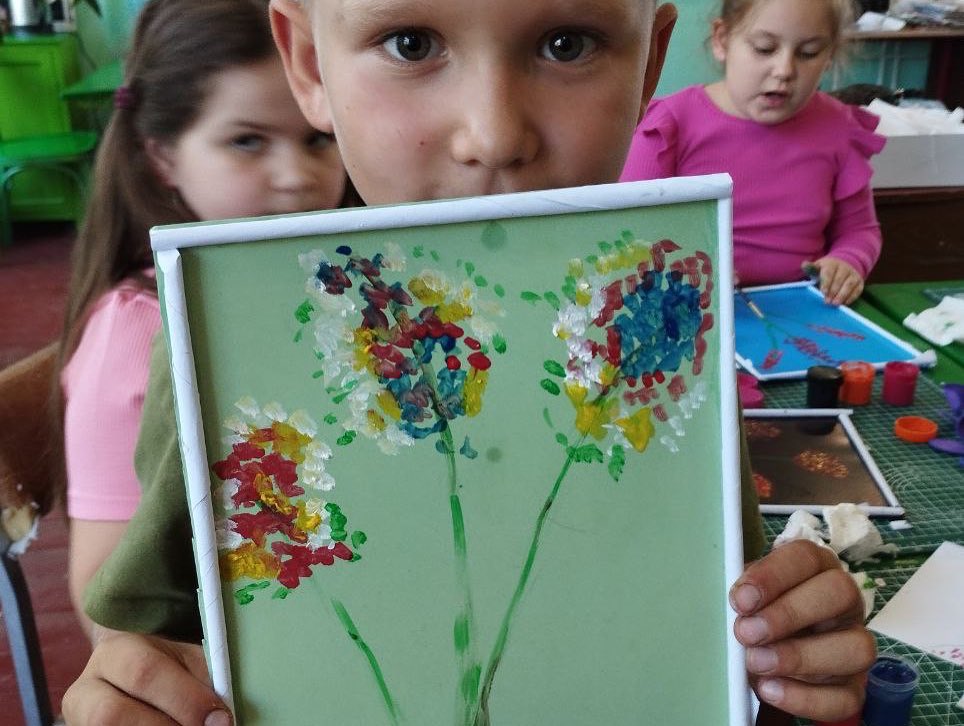 A young boy holding up a picture of flowers.