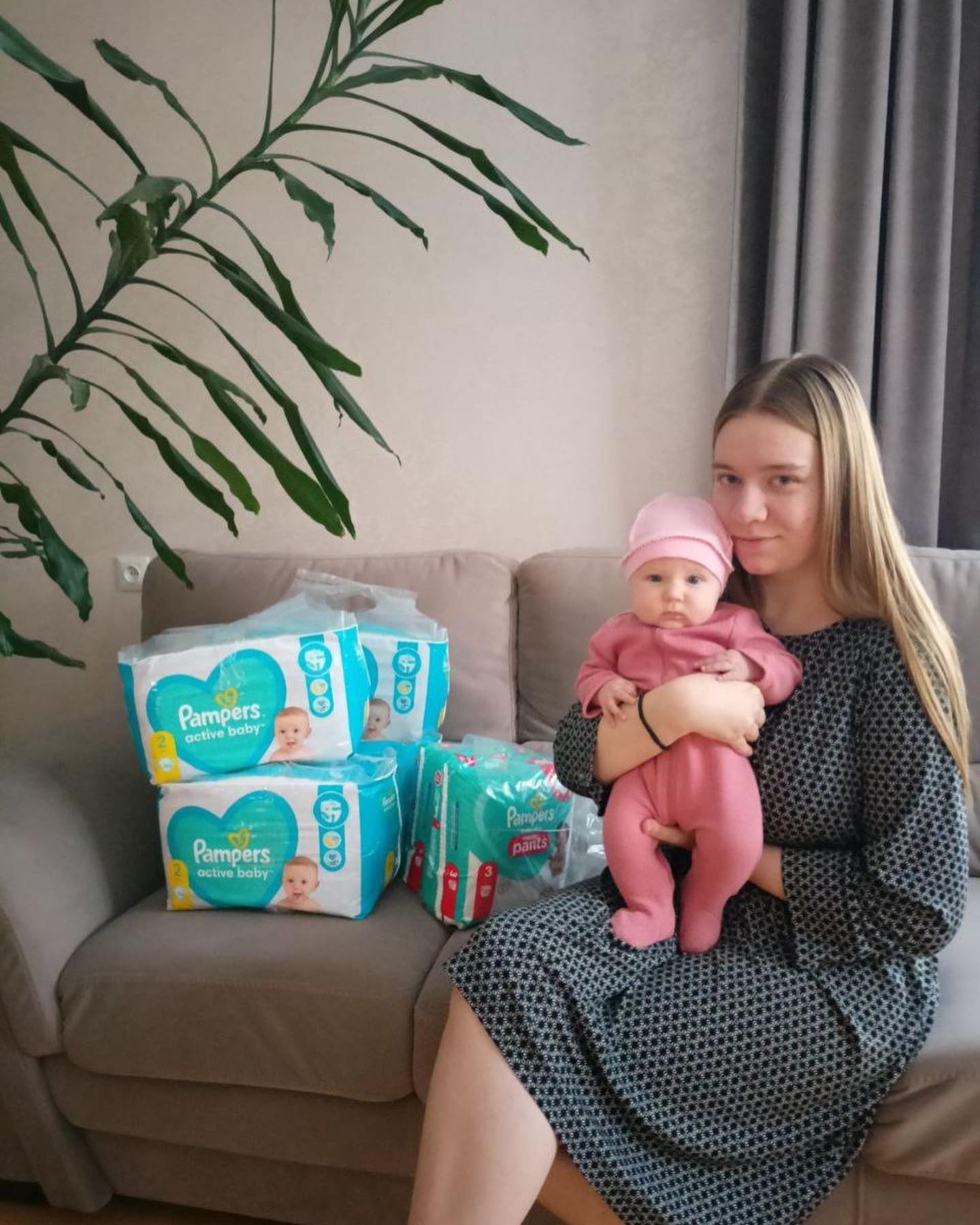A woman with a baby sitting on a couch next to a box of pampers diapers.