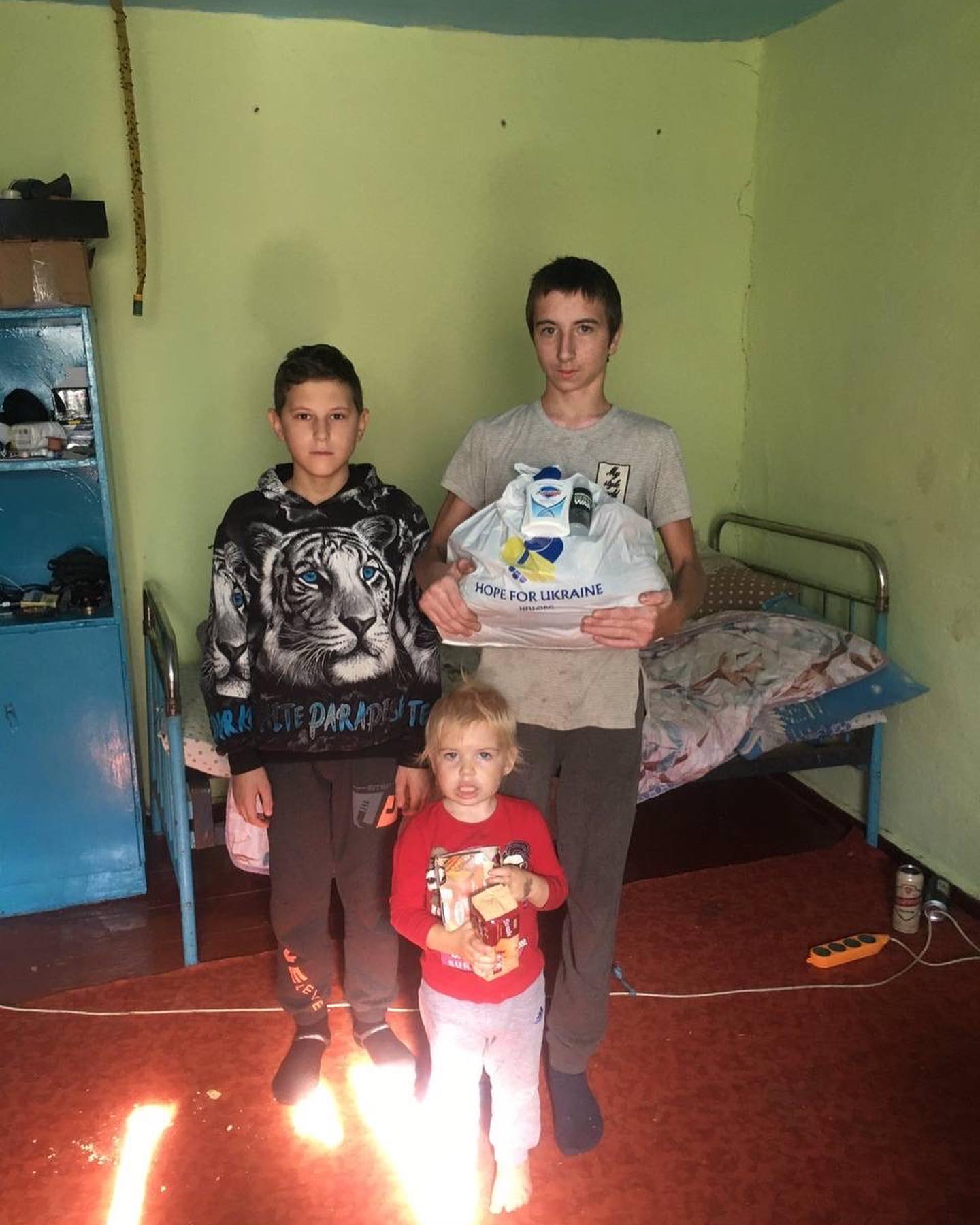 Three children standing in front of a bed in a room.