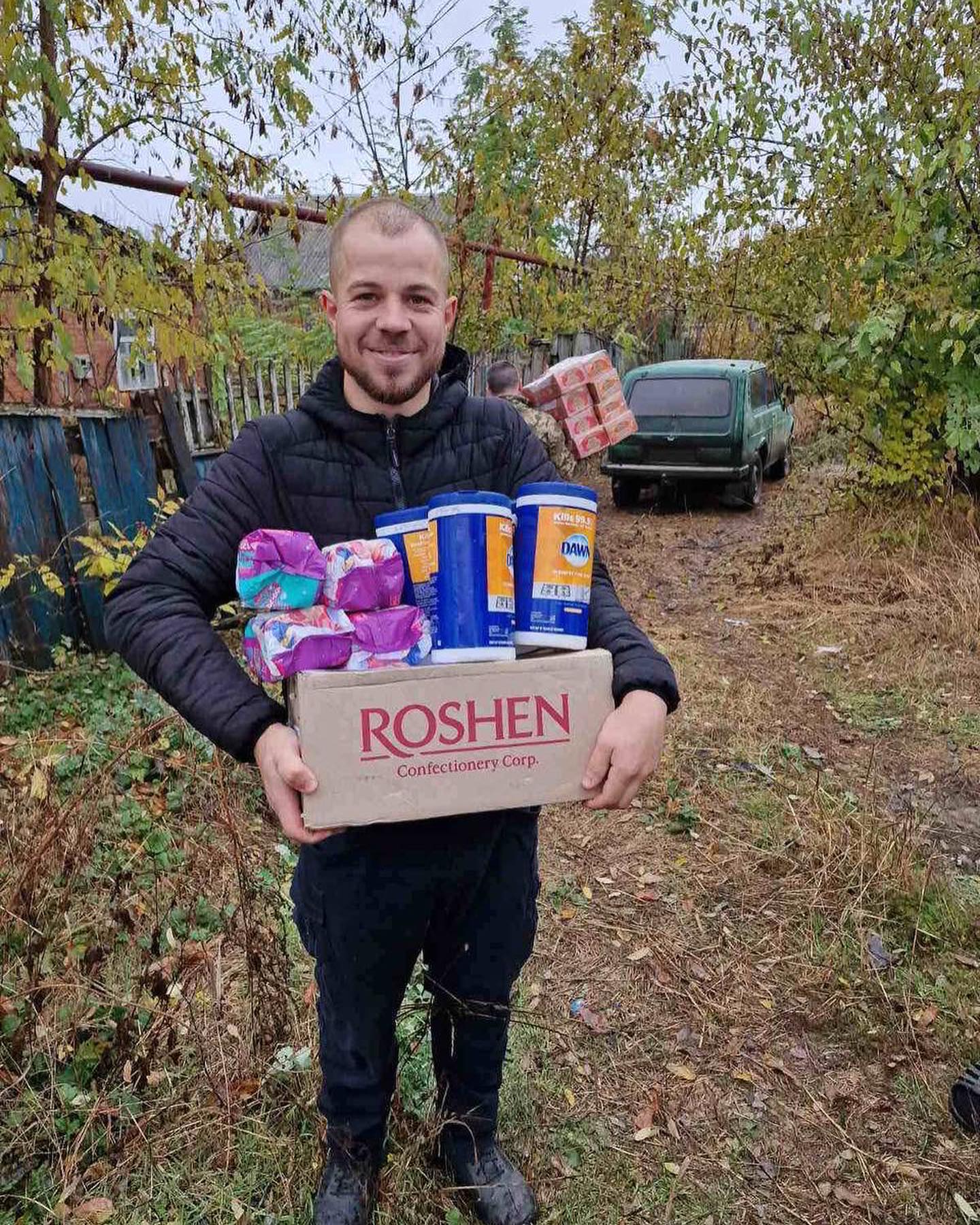 A man holding a box of toiletries in a yard.