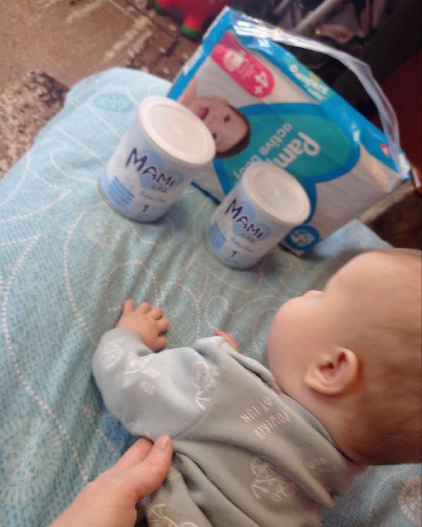 A baby is laying on a bed next to a box of diapers.