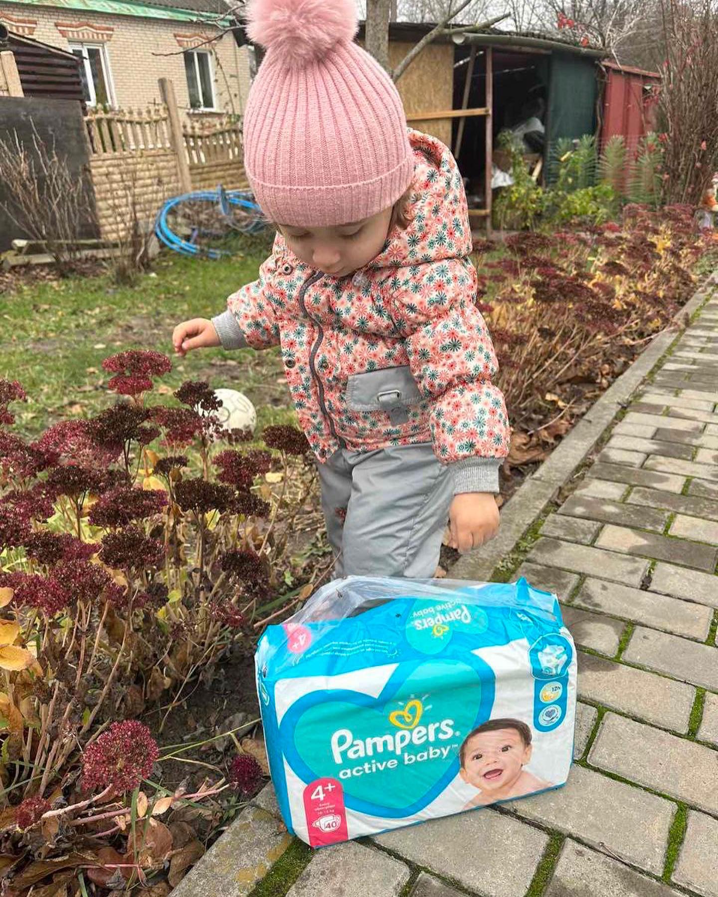 A little girl is standing next to a box of pampers diapers.