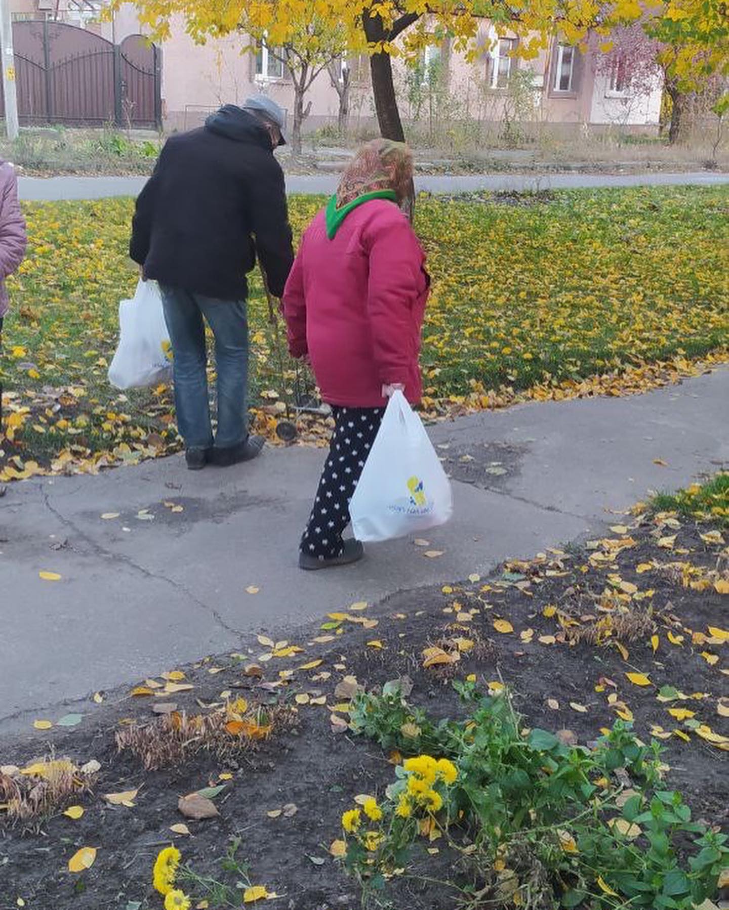 A group of people walking down a sidewalk with bags in their hands.
