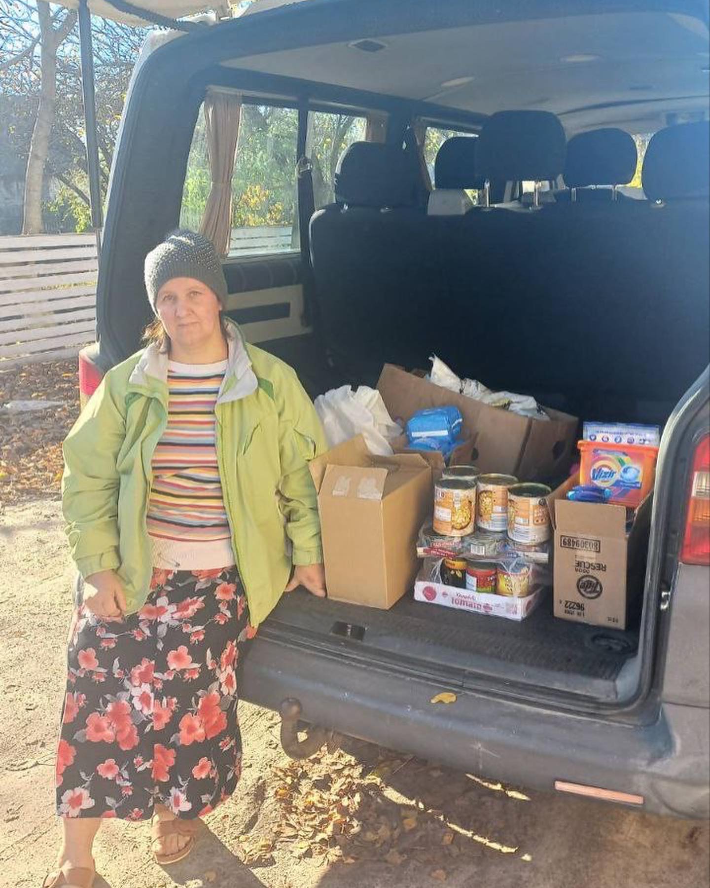 A woman standing next to a van full of food.