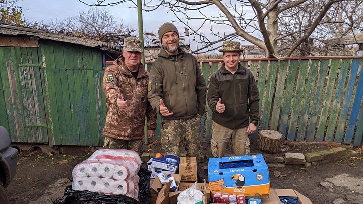 Three men standing next to a pile of food and supplies.