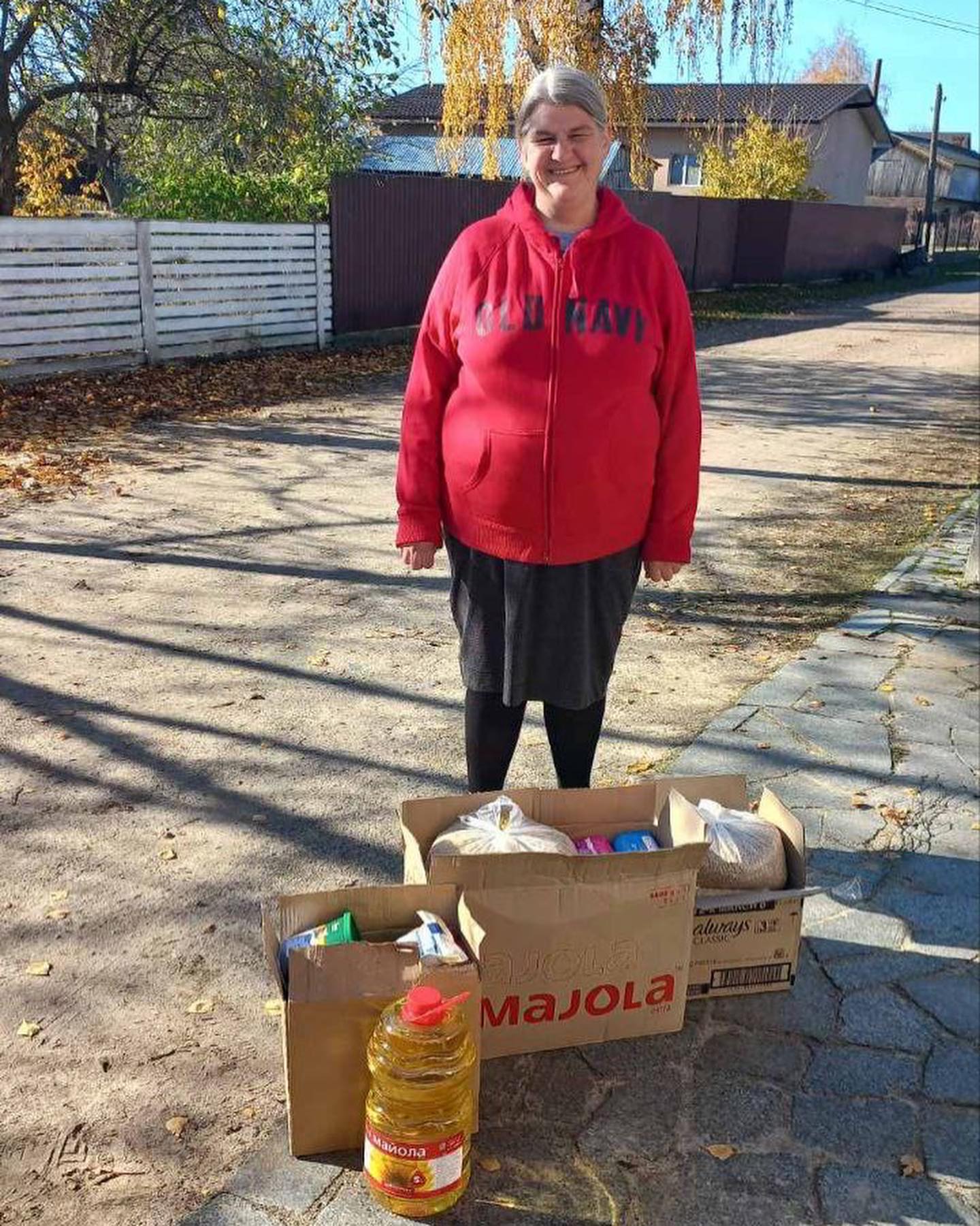 A woman in a red jacket standing next to boxes of food.