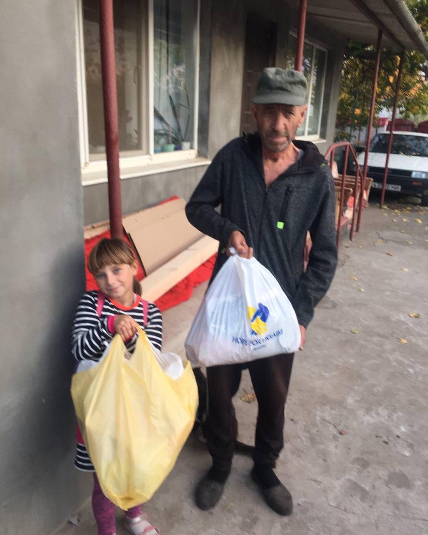 A man and a little girl standing next to each other holding bags.