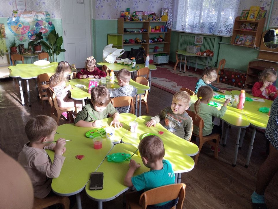 A group of children sitting at tables in a classroom.