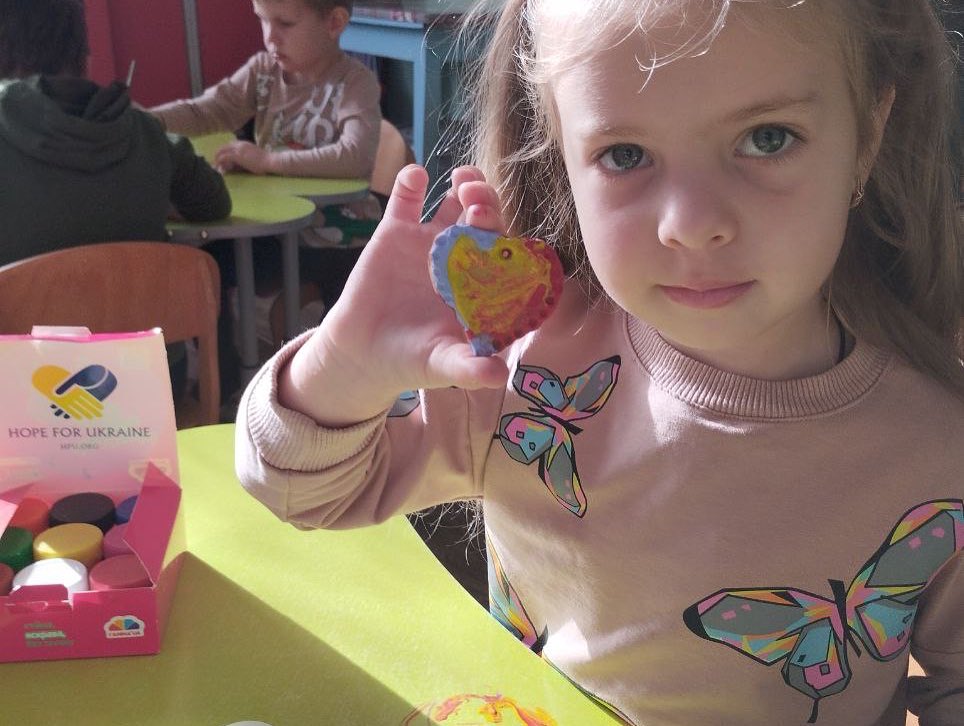 A little girl is holding a heart in front of a table.