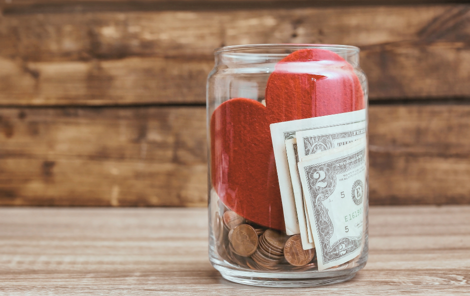 A red heart in a glass jar with money in it.