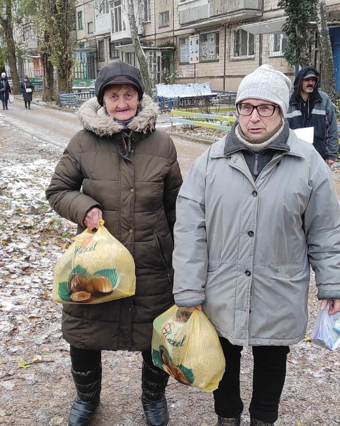 Two women standing on a street with bags of food.