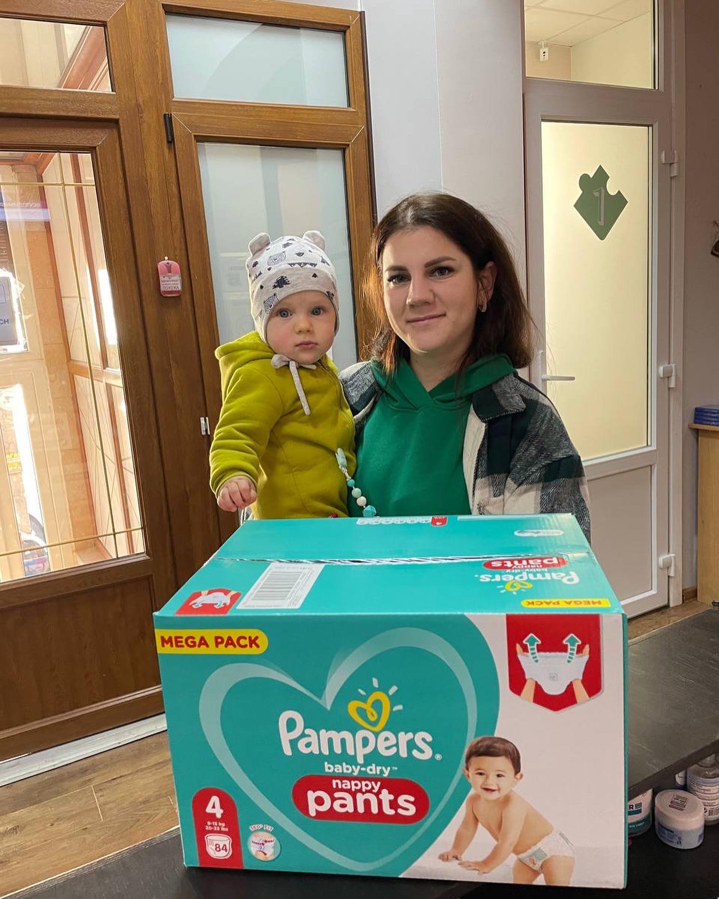 A woman holding a baby in front of a box of pampers diapers.