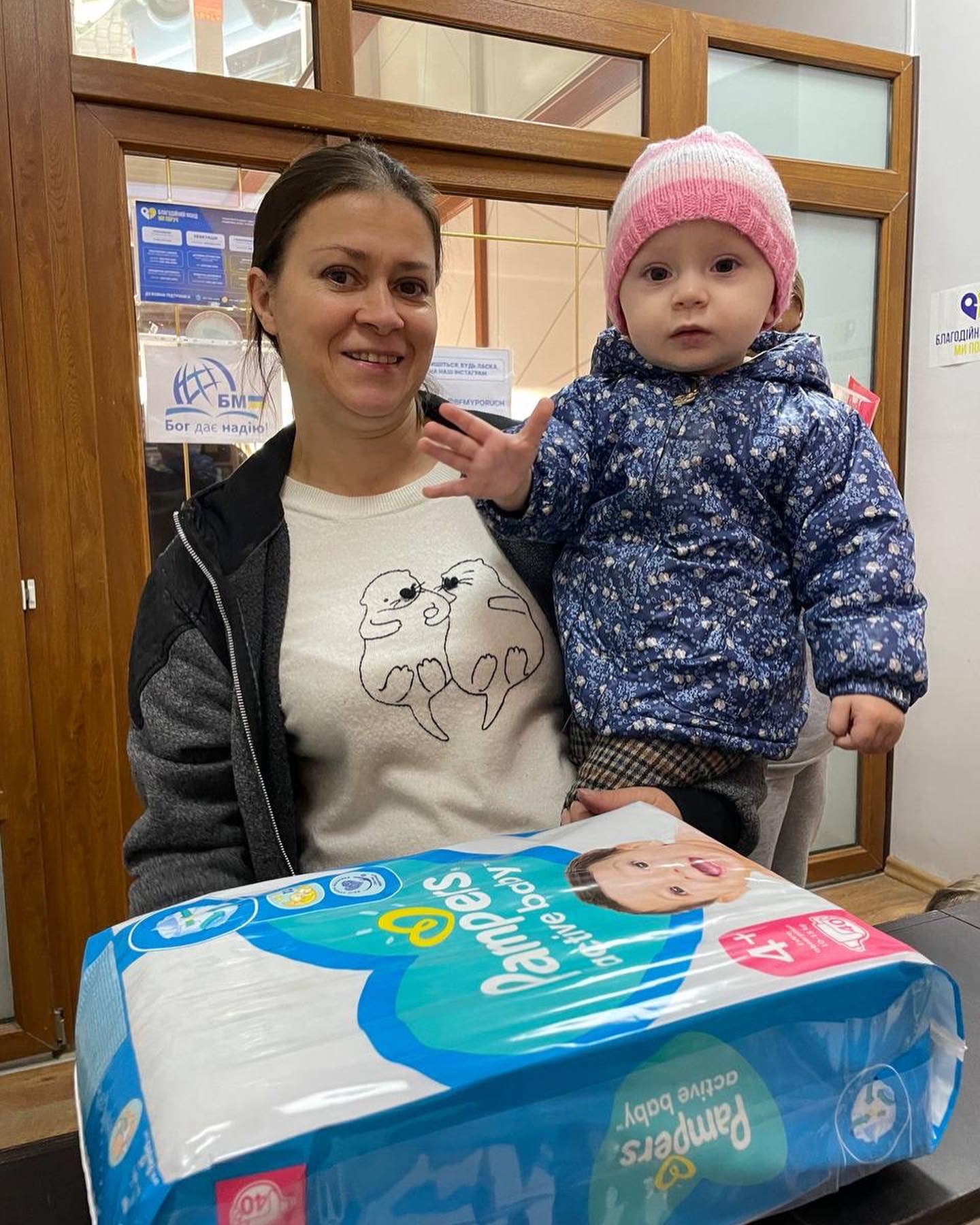 A woman holding a baby next to a box of diapers.