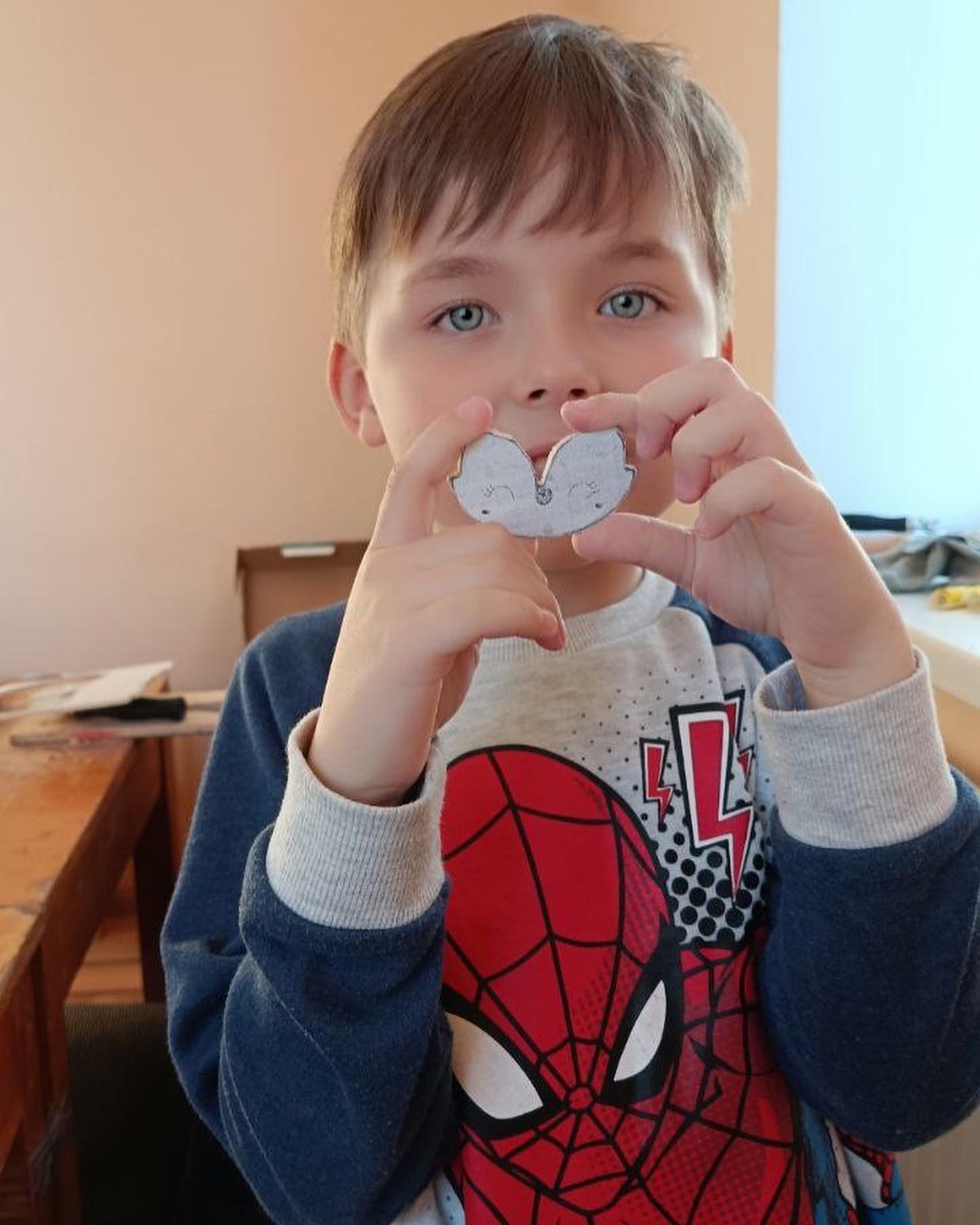 A young boy holding up a heart shaped piece of paper.