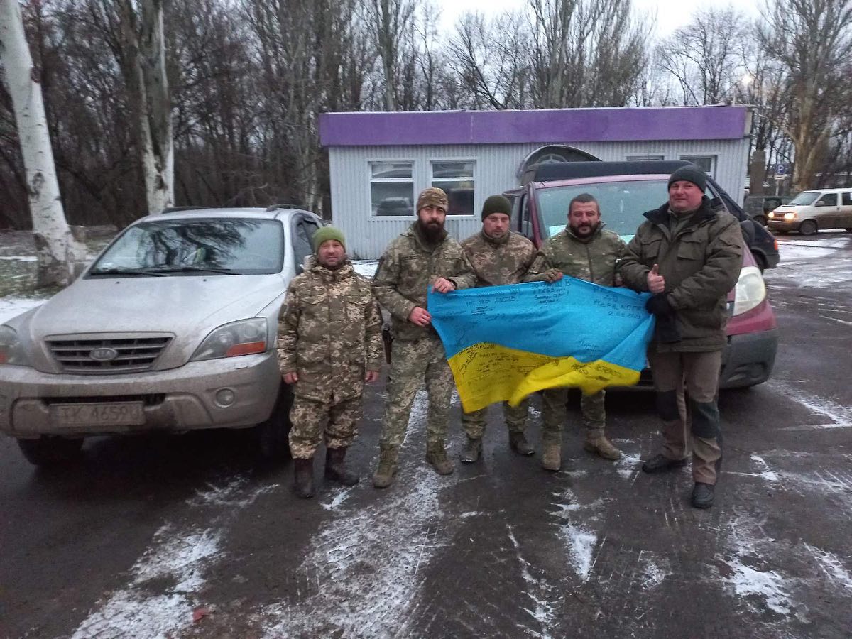 A group of men standing in front of a car with a ukrainian flag.