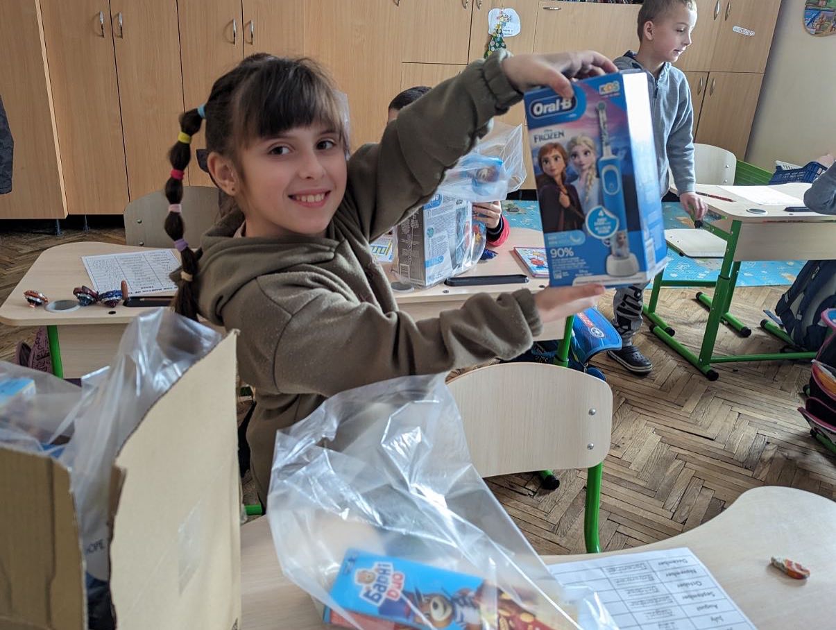 A girl holds up a box of toys in a classroom.